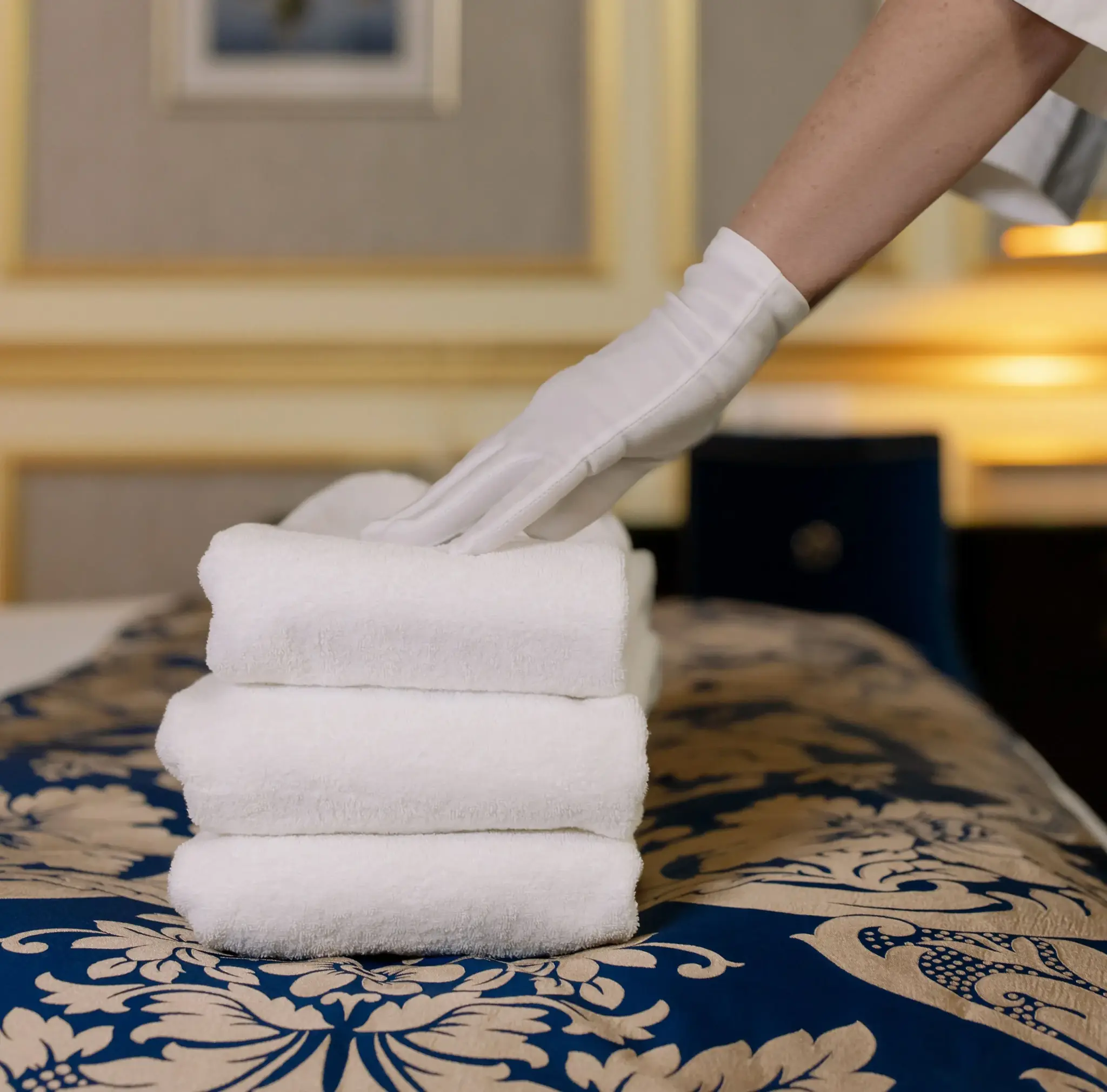 White-gloved hand placing folded towels on a bed